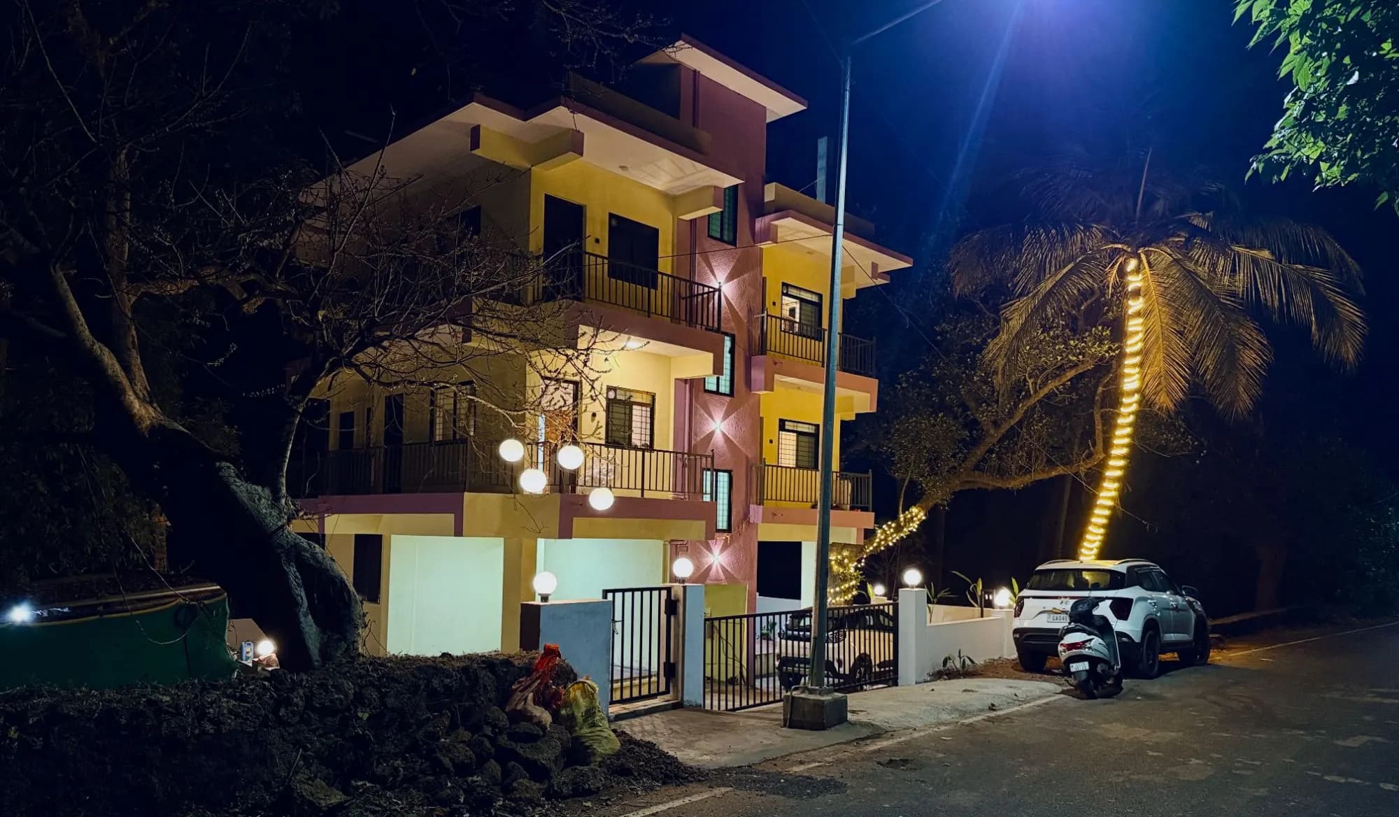 Sadanand Guest House building lit up at night, with a palm tree in fairy lights